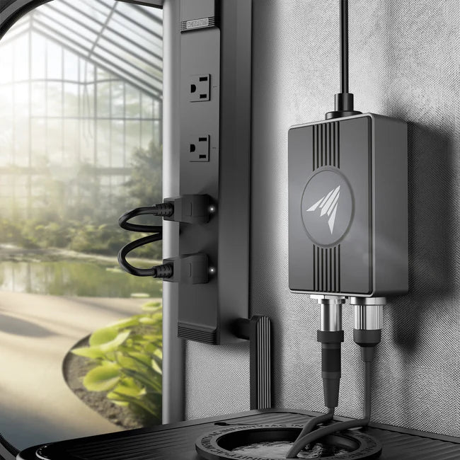 Outdoor irrigation system with controller and nozzles attached to a wall near a window with a view of greenery.